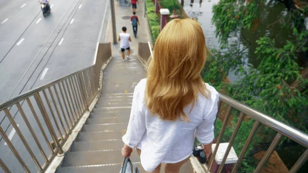 Affascinante giovane donna con i capelli dorati, passeggiando nel centro della città, attraversa il ponte — Foto Stock