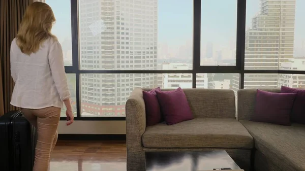 Женщина с чемоданом на фоне небоскребов в панорамном окне — стоковое фото
