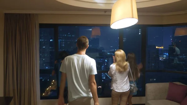 Familia feliz, mujer, hombre en el fondo de los rascacielos en la ventana panorámica por la noche —  Fotos de Stock