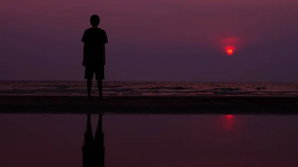 Silueta. solitario asiático joven caminando pacíficamente a lo largo de una playa desierta al atardecer. paisaje marino — Foto de Stock