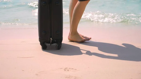 Close-up, female bare feet next to a suitcase on a white beach by the sea. travel concept — Stock Photo, Image