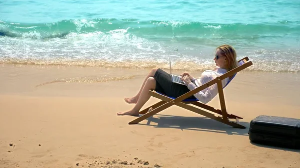 Zakenvrouw werking voort te laptop zittend in een ligstoel aan zee op een wit zandstrand. freelance of workaholism concept. — Stockfoto