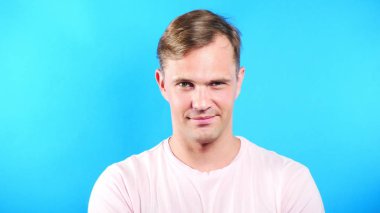 Mavi renkli arka plan üzerinde genç adam. portre. duygu ve hareketleri. yakın çekim. adam cinsel kameraya bakıyor ve onunla birlikte gitmek öneriyor.