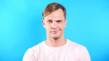 Mavi renkli bir arka plan üzerinde genç adam. portre. duygu ve hareketleri. yakın çekim. Kamera ve sevimli gülümseme adam bakar