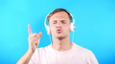 Mavi renkli bir arka plan üzerinde genç adam. portre. duygu ve hareketleri. yakın çekim. adam beyaz kulaklık müzik dinlemek