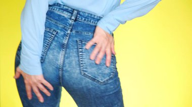 bir kız kot pantolon güzel yuvarlak kalça ile cinsel hareket ediyor. yakın çekim. renkli sarı arka plan