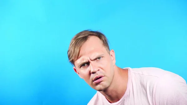 Junger Mann auf blauem Hintergrund. Porträt. Emotionen und Gesten aus nächster Nähe. schaut der Kerl interessiert in die Kamera. Was passiert . — Stockfoto