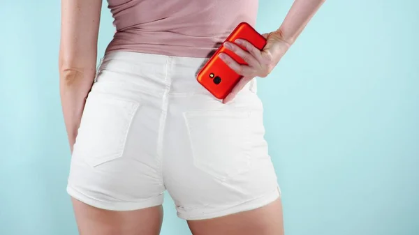Mujer de moda con un teléfono inteligente en sus pantalones cortos de bolsillo. Moda de verano. Vacaciones. fondo de color . — Foto de Stock