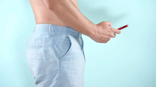 Närbild. Färgstark bakgrund. En ung man i blå shorts använder en röd telefon — Stockfoto