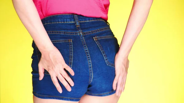 Chica en pantalones cortos pantalones cortos azules. Vista de cerca desde atrás. Estilo fresco de verano. fondo amarillo de color — Foto de Stock