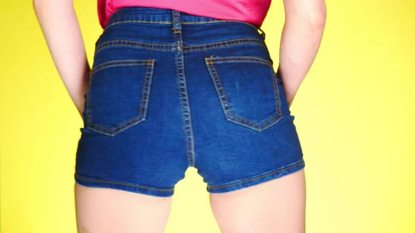 Flicka i kort blå jeansshorts. Närbild från bakom. Sommar fräsch stil. färgad gul bakgrund — Stockfoto