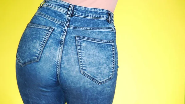Una chica en jeans con hermosas nalgas redondas se mueve sexualmente. Primer plano. fondo amarillo de color —  Fotos de Stock