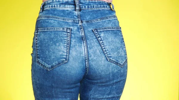 Una chica en jeans con hermosas nalgas redondas se mueve sexualmente. Primer plano. fondo amarillo de color —  Fotos de Stock