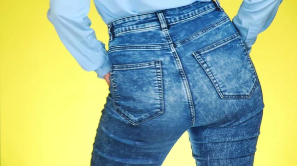 A girl in jeans with beautiful round buttocks is sexually moving. close-up. colored yellow background — Stock Photo, Image
