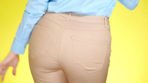 Ein Mädchen in Jeans mit schönem rundem Gesäß ist sexuell bewegend. Nahaufnahme. farbig gelber Hintergrund — Stockfoto