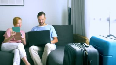 Turizm, online alışveriş turları kavramı. Romantik Çift evde seyahat için hazırlanıyor. Bir dizüstü bilgisayar ve pasaport ellerinde kanepenin üstünde oturmak. Bavulları yakın olmakla birlikte, odaklanmak