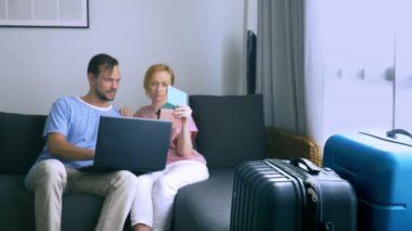 Turizm, online alışveriş turları kavramı. Romantik Çift evde seyahat için hazırlanıyor. Bir dizüstü bilgisayar ve pasaport ellerinde kanepenin üstünde oturmak. Bavulları yakın olmakla birlikte, odaklanmak