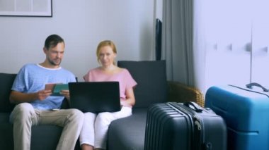 Turizm, online alışveriş turları kavramı. Romantik Çift evde seyahat için hazırlanıyor. Bir dizüstü bilgisayar ve pasaport ellerinde kanepenin üstünde oturmak. Bavulları yakın olmakla birlikte, odaklanmak