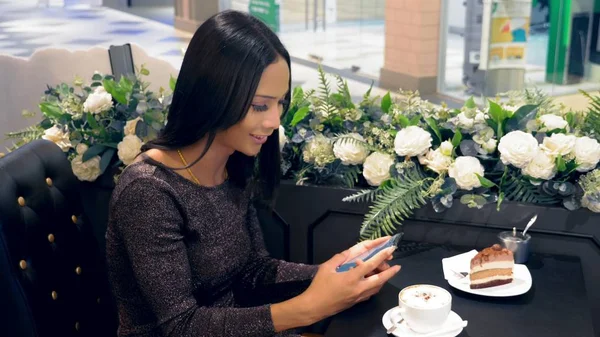 Aantrekkelijke Aziatische meisje ladyboy is glimlachend en met behulp van haar smartphone zittend aan een tafel in een koffieshop — Stockfoto