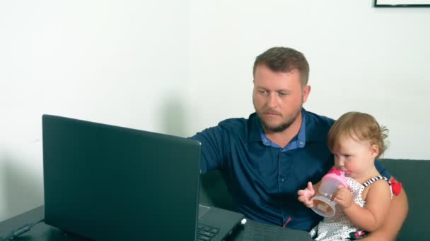 Концепція роботи фрілансера. Щасливий тато працює вдома з ноутбуком, тримаючи дитину на руках . — стокове відео