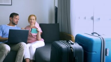 Turizm, online alışveriş turları kavramı. Romantik Çift evde seyahat için hazırlanıyor. Bir dizüstü bilgisayar ve pasaport ellerinde kanepenin üstünde oturmak. Bavulları yakın olmakla birlikte, odaklanmak