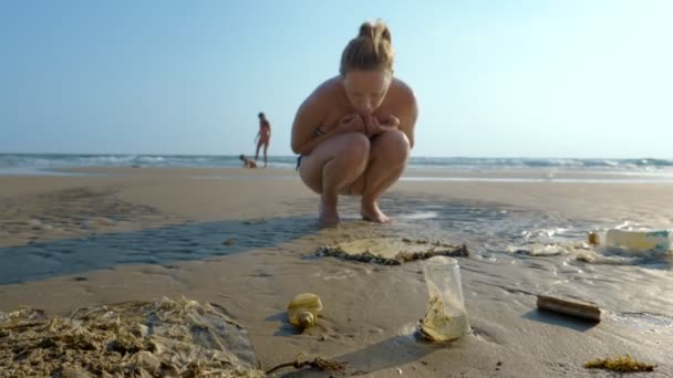 Das Konzept der Umweltverschmutzung. Küstenmüll am Strand bei Ebbe, Touristen betrachten die Gegenstände, die nach Ebbe im Sand liegen bleiben — Stockvideo