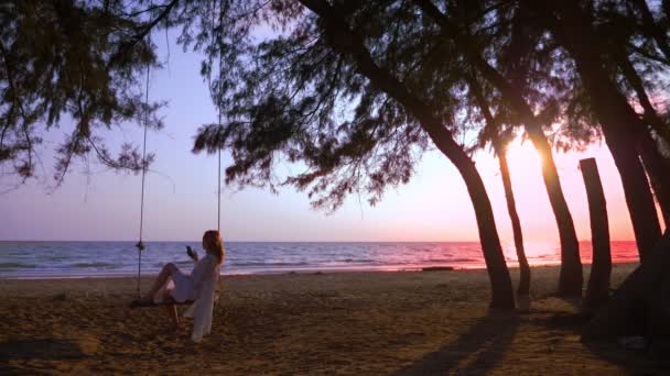 Счастливая блондинка в белом платье и кружевной плащ качается на веревке качели, на пляже у моря . — стоковое видео