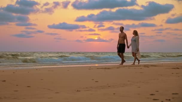 Romantisch paar, Man en vrouw lopen langs het strand bij zonsondergang, hand in hand. — Stockvideo