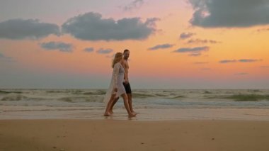 Romantik Çift, erkek ve kadın plaj boyunca el ele tutuşarak batımında, yürümek
