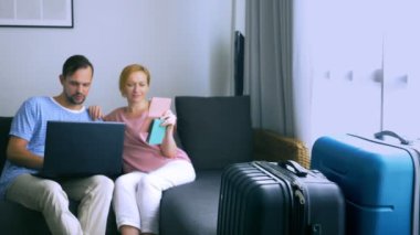 Turizm, online alışveriş turları kavramı. Romantik Çift evde seyahat için hazırlanıyor. Bir dizüstü bilgisayar ve pasaport ellerinde kanepenin üstünde oturmak. Bavulları yakın olmakla birlikte, odaklanmak