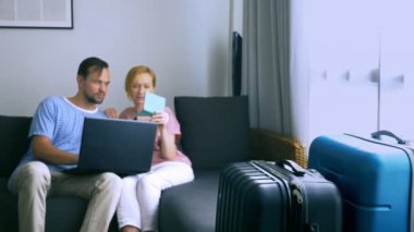 Turizm, online alışveriş turları kavramı. Romantik Çift evde seyahat için hazırlanıyor. Bir dizüstü bilgisayar ve pasaport ellerinde kanepenin üstünde oturmak. Bavulları yakın olmakla birlikte, odaklanmak