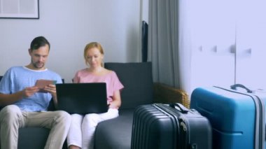 Turizm, online alışveriş turları kavramı. Romantik Çift evde seyahat için hazırlanıyor. Bir dizüstü bilgisayar ve pasaport ellerinde kanepenin üstünde oturmak. Bavulları yakın olmakla birlikte, odaklanmak