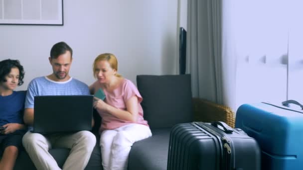 The concept of tourism, online shopping, tours. happy family preparing to travel at home. Sit on the sofa with a laptop and passports in hand. focus on the suitcases — Stock Video