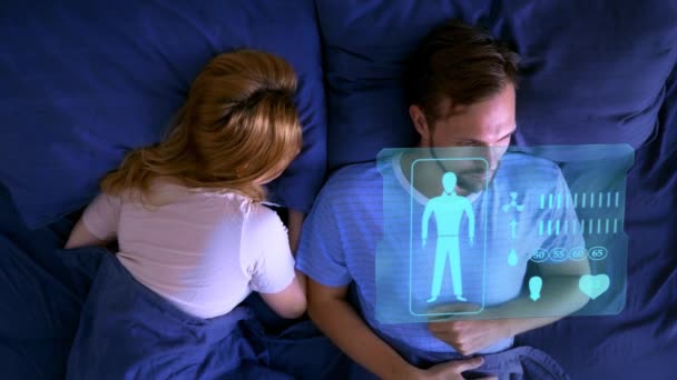 Futuristische concept van slimme gadgets. Smart home, smart bed, man liggend in bed, beheert op een virtueel scherm de functies van de verbetering van de slaap — Stockvideo