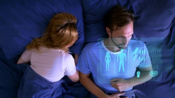 Futuristický koncept inteligentního miniaplikací. Inteligentní domov, inteligentní postel, muž leží v posteli, spravuje na virtuální obrazovce funkce zlepšení spánku — Stock video