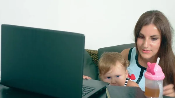 Het concept van vrouwelijke freelance werken. Moderne moederschap. Werkende moeder met een kind aan de tafel. moe, teleurgesteld moeder met een kind in haar armen terwijl u werkt op een laptop. — Stockfoto