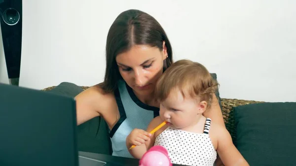 Vrouwelijke freelance werk concept. Moderne moederschap. Werkende moeder met een kind aan de tafel. Drukke vrouw die werkt op een laptop met een baby in haar armen. — Stockfoto
