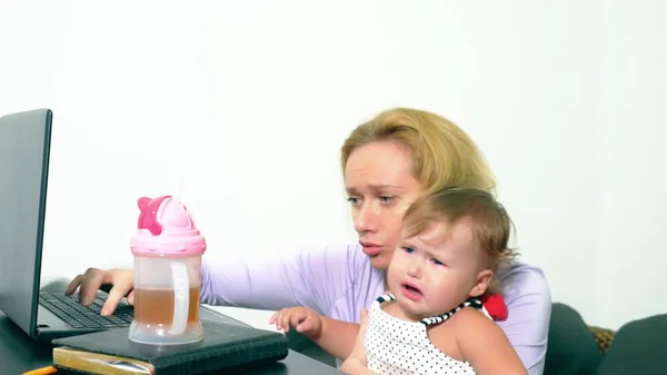 Empresaria molesta sosteniendo a un bebé llorando en sus brazos mientras trabaja en un portátil. Concepto de mamá de carrera, problemas asociados con el trabajo en el hogar — Foto de Stock
