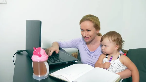 Concepto de mamá trabajadora, freelancing. madre feliz trabajando en casa con el ordenador portátil sosteniendo al bebé en sus brazos . — Foto de Stock