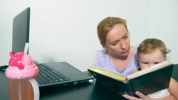 Concepto de mamá trabajadora, freelancing. madre feliz trabajando en casa con el ordenador portátil sosteniendo al bebé en sus brazos . — Foto de Stock