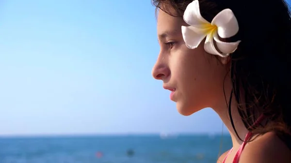 Крупним планом портрет брюнетки з квіткою сливи у волоссі на тропічному пляжі — стокове фото