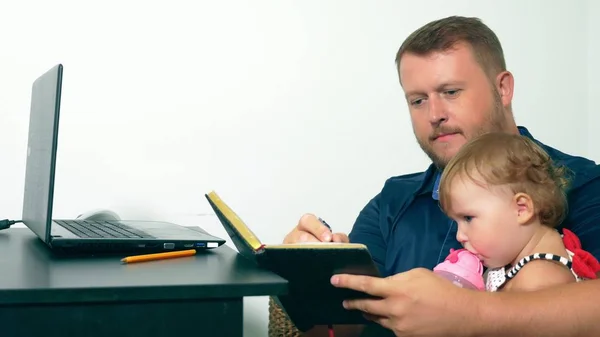 Koncepcja pracy freelancera. Szczęśliwy tata pracuje w domu z laptopem, trzymając dziecko w ramionach. — Zdjęcie stockowe