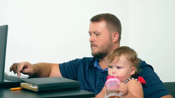Freiberufler arbeiten Konzept. glücklicher Papa, der zu Hause mit einem Laptop arbeitet und das Baby im Arm hält. — Stockfoto