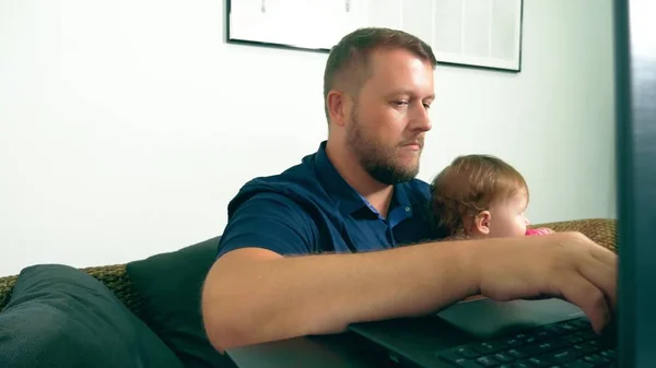 Koncepcja pracy freelancera. Szczęśliwy tata pracuje w domu z laptopem, trzymając dziecko w ramionach. — Zdjęcie stockowe