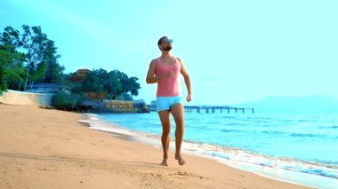 Pembe bir t-shirt ve mavi şort oynak bir yakışıklı adam sevinçle denize çalışır. Denizde ucube