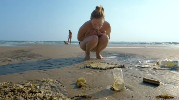 Das Konzept der Umweltverschmutzung. Küstenmüll am Strand bei Ebbe, Touristen betrachten die Gegenstände, die nach Ebbe im Sand liegen bleiben — Stockfoto