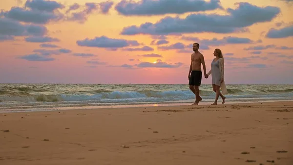 Casal romântico, homem e mulher caminham ao longo da praia ao pôr do sol, de mãos dadas . — Fotografia de Stock