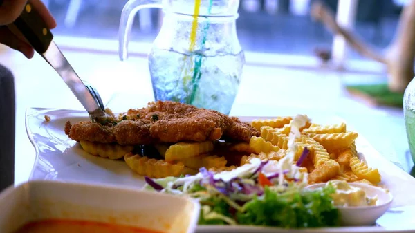 Schnitzel ayam, disajikan dengan kentang goreng dan salad. Seseorang makan kentang goreng dengan garpu di restoran . — Stok Foto