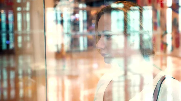 Concepto de compra. mujer joven mirando las mercancías a través del vidrio en la ventana. difuminación — Foto de Stock