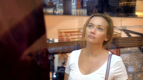 Koncepcja zakupy, Kobieta, patrząc na ubrania na manekiny za szklane gabloty w centrum handlowym — Zdjęcie stockowe